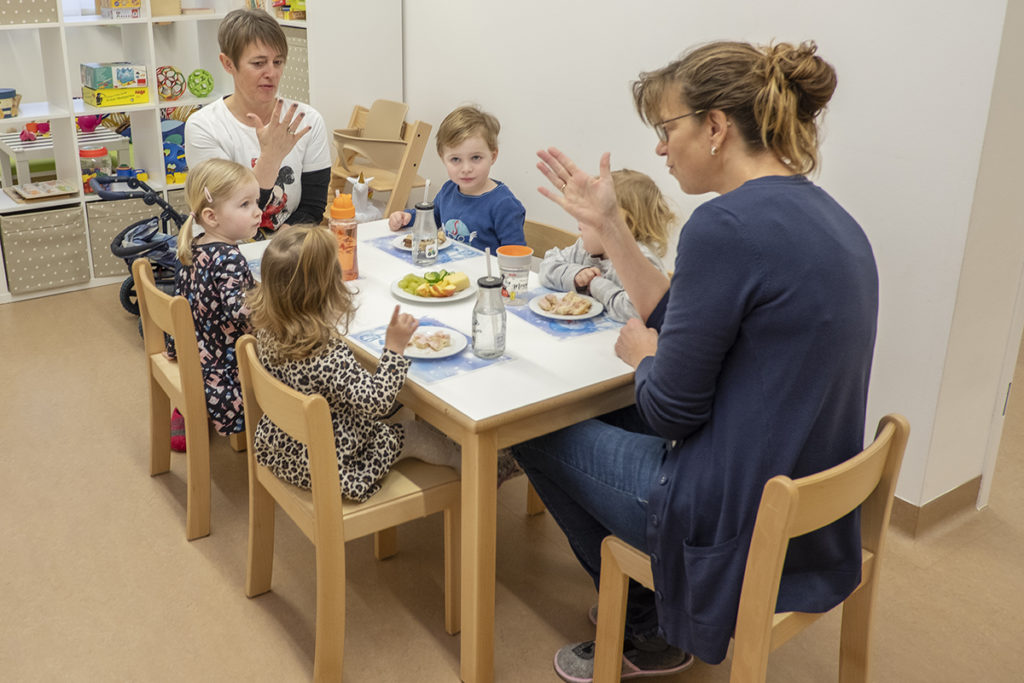 Zwei Frauen sitzen mit vier Kleinkindern an einem Tisch und essen