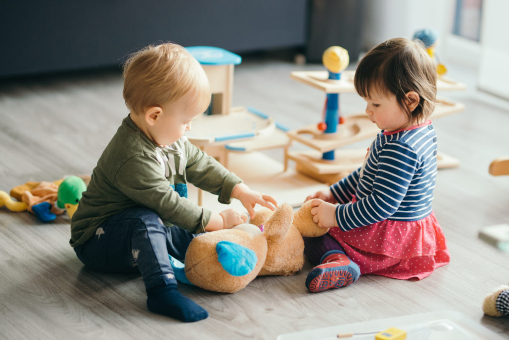 Zwei Kleinkinder spielen mit einem Teddy