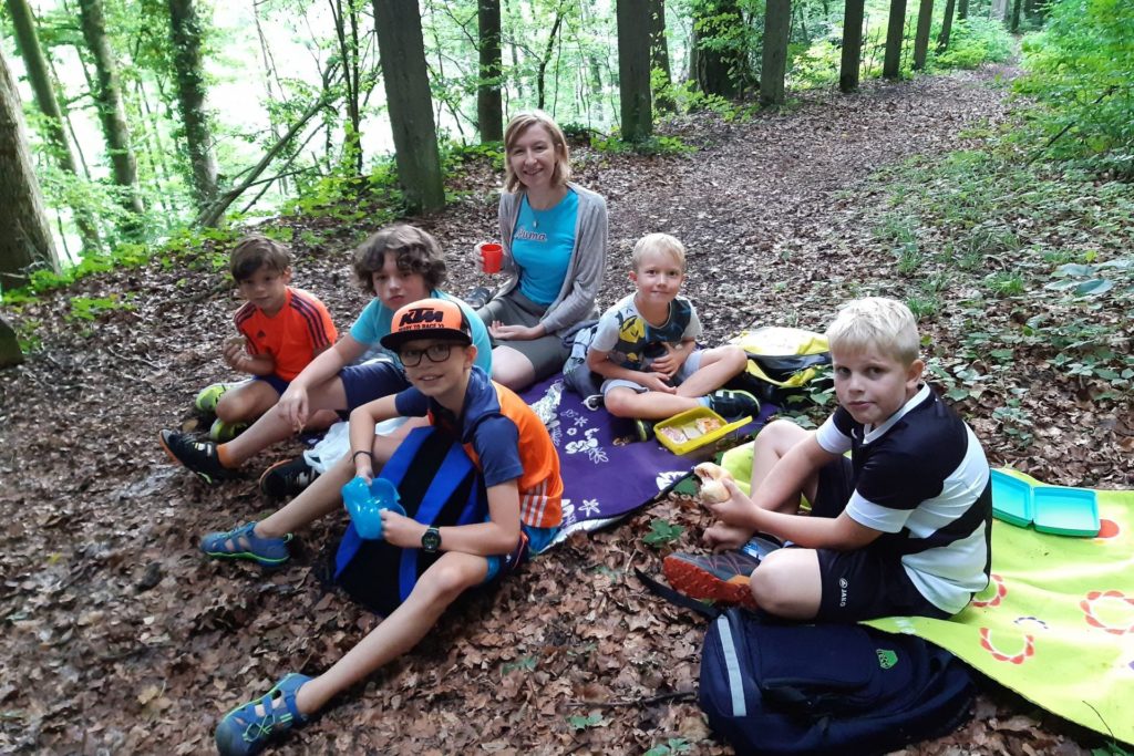 Die Kinder sitzen mit der Tagesmutter im Wald und machen ein Picknick - ein Programmpunkt der Ferienbetreuung mit den Tagesmüttern.